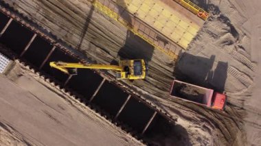 Gündüz vakti güneşli kum ocağında çalışırken kazıcının kir yüklü kamyonunun hava üst görüntüsü.
