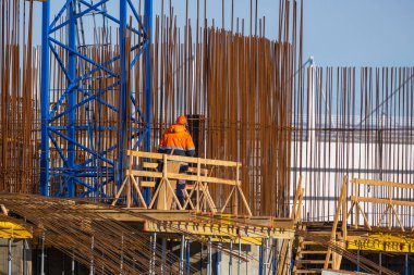 Güneşli bir günde inşaat alanında çalışırken metal direklerin yanında duran koruyucu üniformalı ve miğferli isimsiz müteahhit.