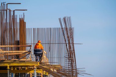 Metal direklere ve bulutsuz mavi gökyüzüne karşı inşaat alanında inşaat yapan isimsiz bir inşaat işçisi.
