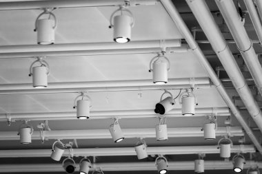 Çağdaş endüstriyel tesisin içindeki boruların yakınındaki beyaz tavanda asılı birçok lambanın altından.