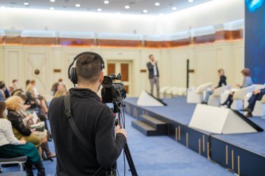 Geniş oditoryumdaki iş semineri sırasında sahnede konuşan insanları çekmek için profesyonel kamera kullanan isimsiz bir adam.