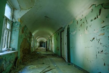 Terk edilmiş binanın içinde yıpranmış duvarlarla kaplı uzun koridorun içi.