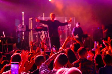 Kimliği belirsiz insanlar müzik şovu sırasında sahneye yakın kırmızı neon ışıklar altında dans ediyor ve kollarını kaldırıyor.