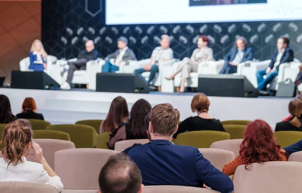 Çağdaş konferans salonundaki iş seminerinde konuşmacıları dinlerken resmi kıyafetli tanınmayan erkek ve kadınların arka planı