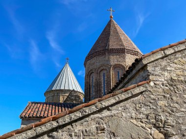 Ortaçağ Gergeti Trinity Kilisesi 'nin aşağısından, Georgia' da güneşli bir yaz gününde mavi gökyüzü ve yıpranmış taş duvarın yanında yer alır.
