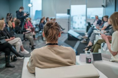 Gündelik kıyafetlerle arka planda oturan ve iş konferansı sırasında hoparlör dinleyen kimliği belirsiz bir erkek var.