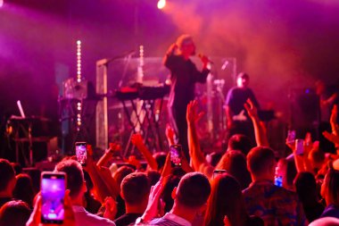 Kimliği belirsiz insanlar müzik şovu sırasında sahneye yakın kırmızı neon ışıklar altında dans ediyor ve kollarını kaldırıyor.