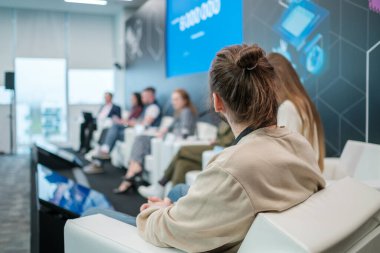 Gündelik kıyafetlerle arka planda oturan ve iş konferansı sırasında hoparlör dinleyen kimliği belirsiz bir erkek var.