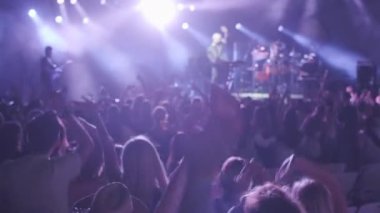 İnsanlar geceleri müzik gösterilerinde grup performansını dinlerken el sallıyor ve el sallıyorlar.