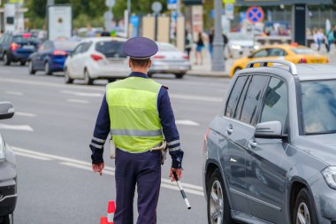 Trafik polisi üniforması ve güvenlik yeleği giymiş kimliği belirsiz bir adam şehir caddesinde arabalarla yol kenarında dikiliyor.