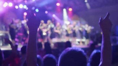 Tanınmayan erkek izleyiciler gece bando performansı sırasında kalabalık içinde dans ediyor ve kollarını kaldırıyor.