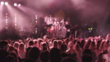 İnsanlar gece geç saatlerde konser sırasında sahnenin yanındaki neon ışıkları altında dans ediyorlar.