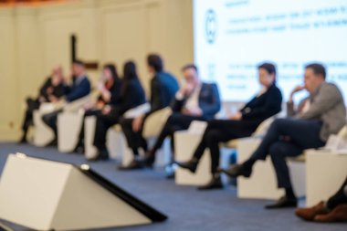 Modern konferans salonundaki iş konferansında büyük ekranın yanında oturan takım elbiseli bir grup bulanık girişimci.