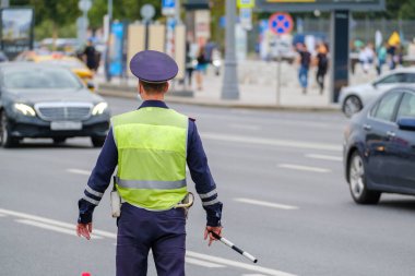 Back view of anonymous man in traffic police uniform and safety vest standing near road with cars on city street