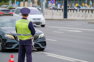 Back view of anonymous man in traffic police uniform and safety vest standing near road with cars on city street