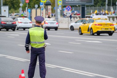 Back view of anonymous man in traffic police uniform and safety vest standing near road with cars on city street