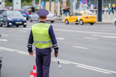 Back view of anonymous man in traffic police uniform and safety vest standing near road with cars on city street