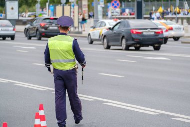 Trafik polisi üniforması ve güvenlik yeleği giymiş kimliği belirsiz bir adam şehir caddesinde arabalarla yol kenarında dikiliyor.
