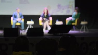 Hoparlör dinleyen iş adamları bulanık. Sonra da loş oditoryumdaki iş seminerinde seyircilerin önünde otururken alkışlıyorlar.