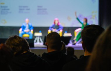 Loş oditoryumdaki iş seminerinde seyirci önünde otururken hoparlör dinleyen bulanık iş adamları