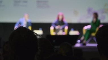 Hoparlör dinleyen iş adamları bulanık. Sonra da loş oditoryumdaki iş seminerinde seyircilerin önünde otururken alkışlıyorlar.