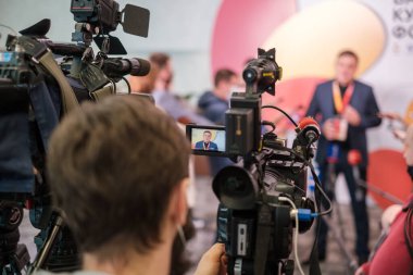 Profesyonel kamerayla iş konferansı sırasında erkek girişimcinin röportaj yaptığı videoyu kaydeden isimsiz bir adamın yumuşak odağı.