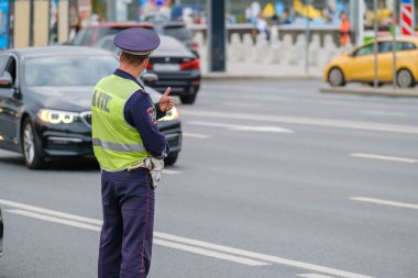 Back view of anonymous man in traffic police uniform and safety vest standing near road with cars on city street