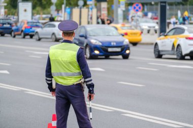 Trafik polisi üniforması ve güvenlik yeleği giymiş kimliği belirsiz bir adam şehir caddesinde arabalarla yol kenarında dikiliyor.