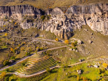 Gürcistan 'ın kırsal kesimlerinde güneşli bir günde sert kayalara oyulmuş Vardzia mağara manastırının insansız hava görüntüsü.