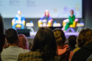 Sahnenin bulanık arka planında karanlık oditoryumda otururken hoparlörleri dinleyen tanınamayan insanlar