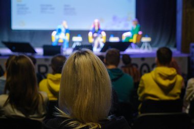 Sahnenin bulanık arka planında karanlık oditoryumda otururken hoparlörleri dinleyen tanınamayan insanlar