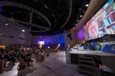 Moskova - 7 Aralık 2021: Geniş salondaki iş konferansı sırasında sahnenin yanındaki sandalyelerde oturan ve çevrimiçi konuşmacıları dinleyen bir kalabalık