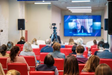 Kırmızı deri koltuklarda oturan ve online iş semineri sırasında hoparlörlerin video konuşması yapan tanınmamış izleyiciler.
