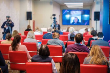 Dar oditoryumdaki iş seminerinde kameramanlar televizyon için video çekerken insanlar çevrimiçi hoparlör dinliyorlar
