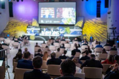 Modern salondaki iş seminerinde sandalyelerde otururken çevrimiçi konuşmacıları dinleyen isimsiz girişimcilerin yumuşak odağı