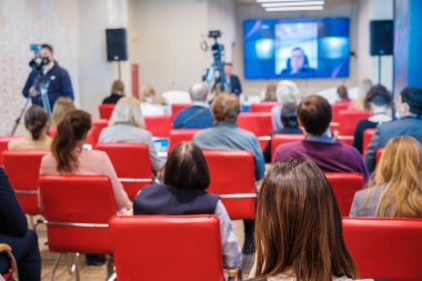 Dar oditoryumdaki iş seminerinde kameramanlar televizyon için video çekerken insanlar çevrimiçi hoparlör dinliyorlar
