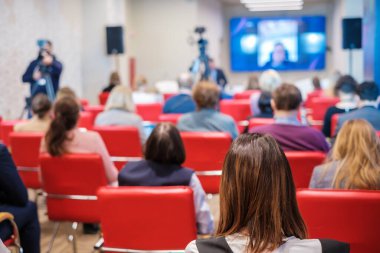 Dar oditoryumdaki iş seminerinde kameramanlar televizyon için video çekerken insanlar çevrimiçi hoparlör dinliyorlar