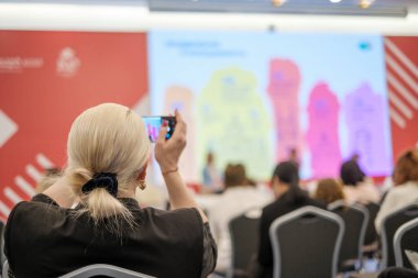 Geniş salondaki iş semineri sırasında bir kadının telefon kullanarak uzman konuşmasını kaydetmesi.