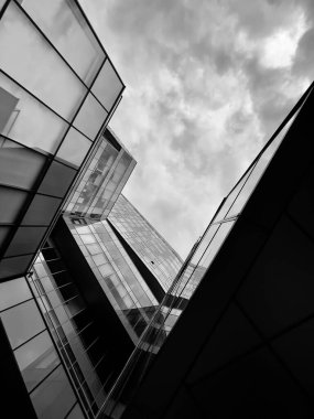 Bulutlu gökyüzünün altında cam pencereleri olan modern binanın modern mimari tasarımının altından siyah ve beyaz