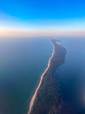 Mavi gökyüzünün altında, okyanusun mavi sularında yemyeşil ağaçlarla kaplı uzak yeşil kumsalın zemininden