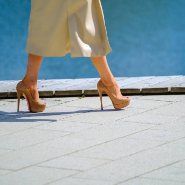 Yüksek topuklu ayakkabılı, şık elbiseli, güneşli yaz gününde mavi duvarda yürüyen anonim bir kadın.