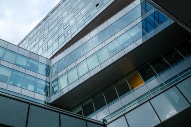 Şehir caddesinde bulutlu gökyüzüne karşı cam duvarları ve pencereleri olan çağdaş binanın altından