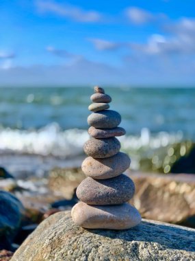 Güneşli bir günde, dalgalı mavi deniz dalgalarına karşı kayaların üzerinde yumuşak çakıl taşları yığını meditasyonu.