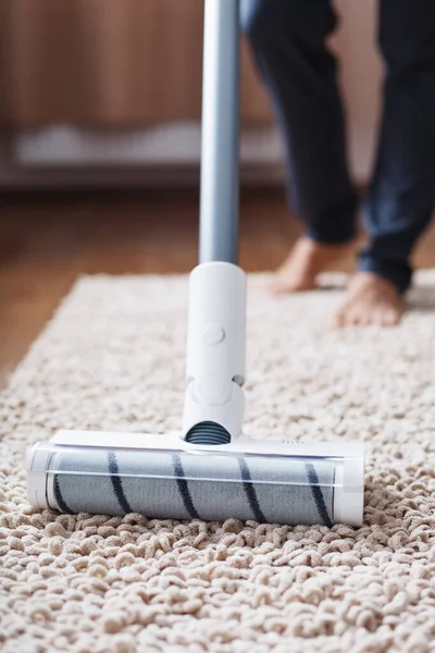 A cordless vacuum cleaner cleans the carpet in the living room with the bottom of the legs.