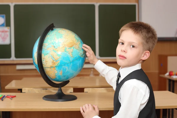 Мальчик указывает на глобус в классе — стоковое фото