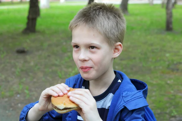 Garçon manger hamburger dans le parc — Photo