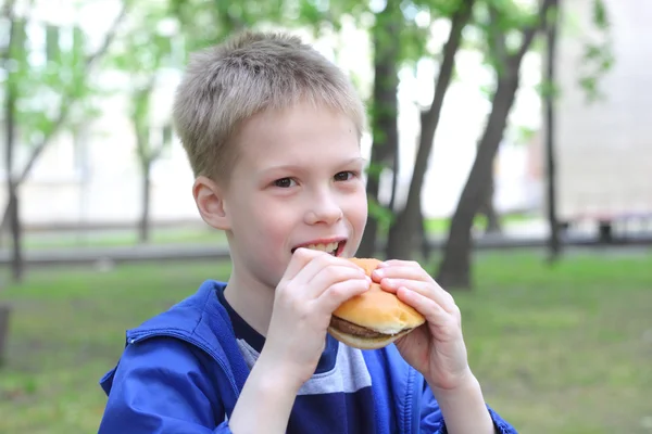 公園でハンバーガーを食べる少年 — ストック写真