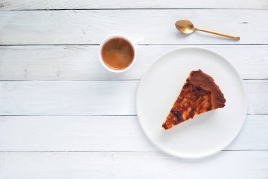 Tabakta bir dilim soğanlı turta, beyaz ahşap arka planda bir fincan kahve ve kaşık, üst manzara, kopyalama alanı.