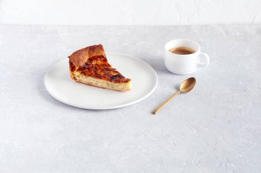 Tabakta bir dilim soğanlı turta, bir fincan kahve ve gri arka planda kaşık, yan görüş.