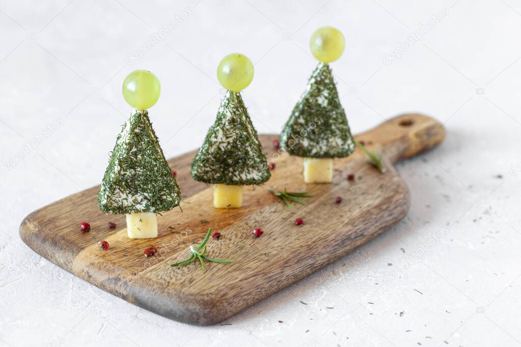 appetizer of new year trees made of cheese and decorated with dill and grapes, easy cooking, on the wooden cutting board, side view